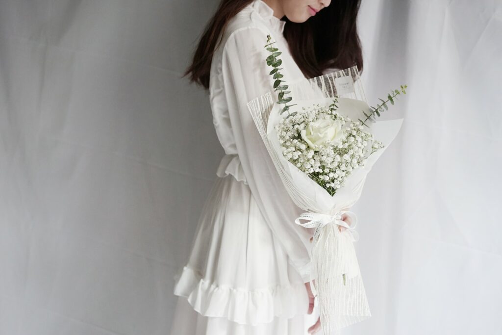 ผู้หญิงผมยาวใส่ชุดขาวถือช่อดอกกุหลาบขาว